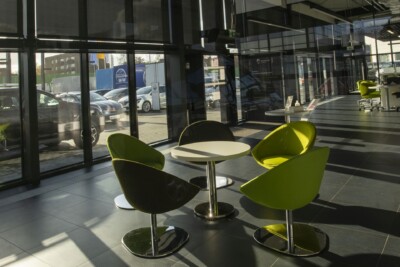 Refleksole w showroomie w Polsce na oknach. Prze okna wpada słońce. W pokoju są kolorowe krzesła i stół.